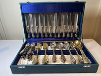Full set of antique gold plated flatware including knives, forks, spoons, and serving pieces arranged inside turquoise flatware box with blue velvet and satin linings.