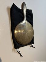 Back view of large sterling silver handheld vanity mirror on black velvet drawstring bag, showing engraved monogram and vertical line texture