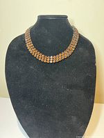 Brown crystal choker necklace displayed on a black bust stand.