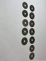 Full view of the 12 antique Chinese copper coins arranged in two parallel vertical rows on a plain background. Each coin has a square hole in the center and visible inscriptions.
