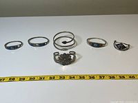 Full view of all 6 silver alpaca Mexico bracelets and bangles arranged in a row with measuring tape for scale