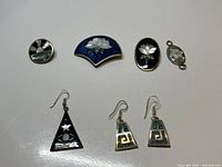 Photo of seven Mexico alpaca silver jewelry pieces including brooches, pendants, and earrings laid flat on white background.