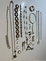 Full overview of silver jewelry items laid out on flat surface showing various necklaces, bracelets, earrings, rings and hairpins.