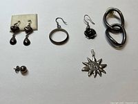 Several sterling silver jewelry pieces including earrings and a sun pendant displayed on white background.