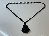 Full view of the black obsidian beaded necklace with the Laughing Buddha pendant attached, laid out flat.