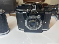 Front view of the black Whitehouse Beacon II film camera showing lens and shutter with 'Beacon' branding.