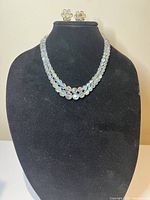 Front view of the black display bust showing the three-strand Aurora Borealis crystal necklace and matching flower-shaped earrings on top.