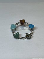 Front view of circular silver brooch showing abalone shell and four multi coloured stones set in twisted silver design.