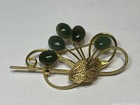 Front view of vintage golden brooch showing floral design and green nephrite jade stones.