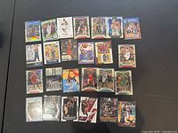 Photo showing 25 basketball trading cards laid out on a dark surface, various teams and players visible, includes holographic and special edition cards.