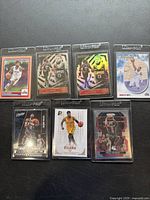Seven collectible Paul George basketball cards, each in protective sleeves and arranged in two rows on black surface