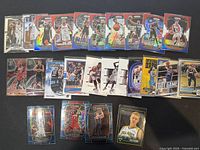 Wide view photo of 25 basketball trading cards arranged on flat surface showing different players, colors, and holographic elements.