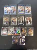 Photo showing 13 Carmelo Anthony basketball trading cards laid out on a dark surface, each card in protective sleeve, featuring Panini and Donruss branding and different designs including holographic and action shots.