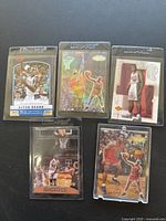 Photo showing five Elton Brand basketball trading cards in individual protective plastic cases on a dark surface. Cards feature various images and designs.