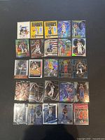 Photo showing 25 basketball trading cards laid out, featuring various holographic and foil designs, each sleeved individually.