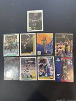 Photo of 9 Shawn Kemp basketball trading cards spread out on a black surface. Cards feature Seattle Supersonics team colors and logos, with varying designs and conditions.