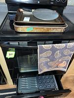 Baking sheets and roasting pan stacked on stove top, muffin tin on oven lower rack, kitchen towel hanging on oven door