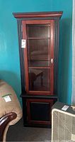 Front view of the tall wooden display cabinet with glass door and closed bottom door, showing some wear and tear.