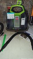 Front view of Bissell Little Green ProHeat Pet carpet cleaner showing the control instructions sticker, hose attachment and Bissell logo.