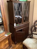 Full view of the small wooden china cabinet, showing upper glass paneled doors and lower wooden doors with one open