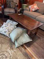 Coffee table placed between upholstered armchair and sofa. Four throw pillows arranged on floor beside table, two floral pattern and two solid green.
