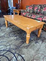 Full view of pine coffee table beside floral couch on patterned rug showing table size and shape.