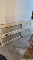 Full view of old vintage painted door showing two large rippled glass panels, wood panels, peeling white paint, and floor setting.