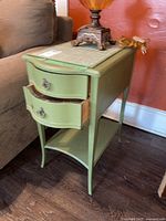 Side view of one green painted vintage side table with two drawers open showing dovetail joinery, decorative metal handles, lower shelf, curved legs.