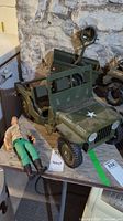 Side angle view of the green G.I. Joe Jeep model 7000 with white star on hood and accompanying Rock N' Roll figurine lying next to it, showing condition and missing tailgate piece.