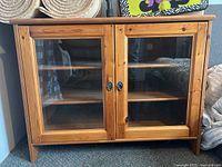 Front view of wooden IKEA cabinet with two glass doors and metal ring handles.