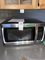 Front angle of RCA microwave showing stainless steel exterior and door with mesh window, placed on a kitchen counter under cabinets.
