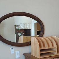Oval mirror mounted on wall above a wooden desk organizer with multiple slots.