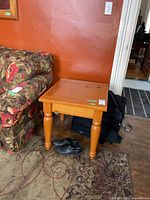 Pine end table positioned near a floral patterned couch, showing the turned legs and natural pine finish, with shoes underneath.