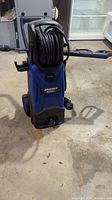 Front view of blue Simoniz pressure washer with hose coiled on front.