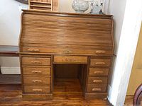 Front view of wooden roll top desk with roll top closed, showing six drawers on each side and center drawer.