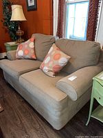 Sklar Peppler two-seater sofa with beige upholstery and two polka dot patterned throw pillows, positioned in a living room with orange walls and wooden floor.