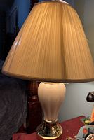 Lit cream ceramic lamp with pleated cream shade, showing detail of pleats and lamp base with brass accents.