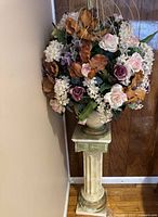 Full view of artificial flower arrangement and vintage column stand showing flower colors and stand design.
