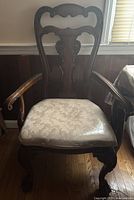 Wooden dining chair with dark carved wood backrest and armrests, patterned cushioned seat in pale fabric