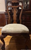 Front view of wooden dining room chair showing the carved wooden backrest and cushioned seat.