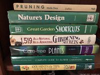 Photo showing seven assorted gardening books stacked with titles visible, covering topics from pruning to garden secrets and tips.