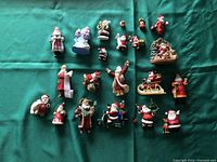 Photo showing a collection of 19 assorted Hallmark Santa Claus ornaments laid out on green fabric background.