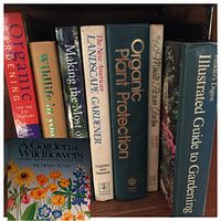 Eight hardcover gardening books arranged vertically on a bookshelf showing titles related to organic gardening, wildlife, wildflowers, gardening techniques, landscape design, floral arranging, and plant protection.