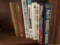 Seven hardcover home repair and DIY books on a wooden shelf, titles visible on spines.