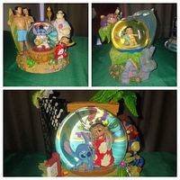 Three different Lilo and Stitch themed snowglobes displayed on a dark cloth background showing characters such as Lilo, Stitch, Nani, Jumba, Pleakley in detailed multi-figure bases, with glass globes containing figurines with snow or glitter effect.