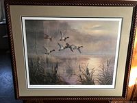 Large rectangular framed print showing mallards flying over a marsh at sunset, with surrounding matting and dark wood frame.