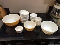 Three glass mixing bowls in graduated sizes with amber or white exteriors and assorted white ceramic ramekins of various sizes.