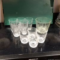 Lead crystal ice tub and eight glasses (four old-fashioned and four tall) displayed on black surface with green background.