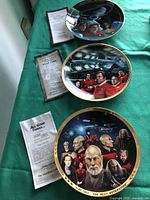 Three Star Trek collectible plates on a green cloth with accompanying certificates detailing the episodes or movies each plate represents