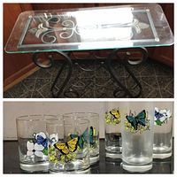 Top image shows wine table with glass etched top with floral and scroll designs and black metal base with curled legs and wine bottle holders. Bottom image shows close up of 3 old fashioned and 3 iced tea glasses decorated with colorful butterflies and flowers.